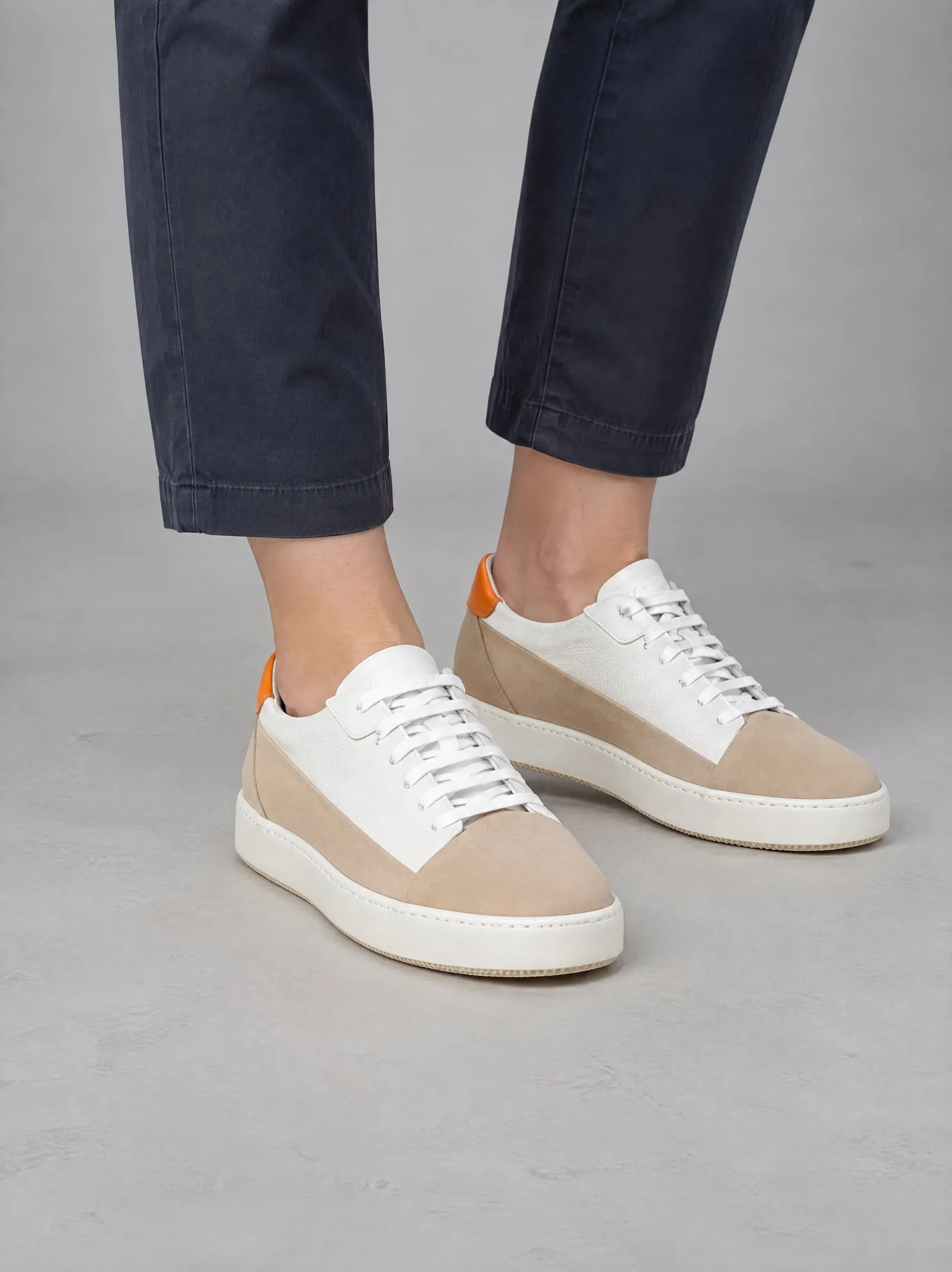 Iris wearing the sand suede court sneakers, close up, facing the camera, in a grey studio