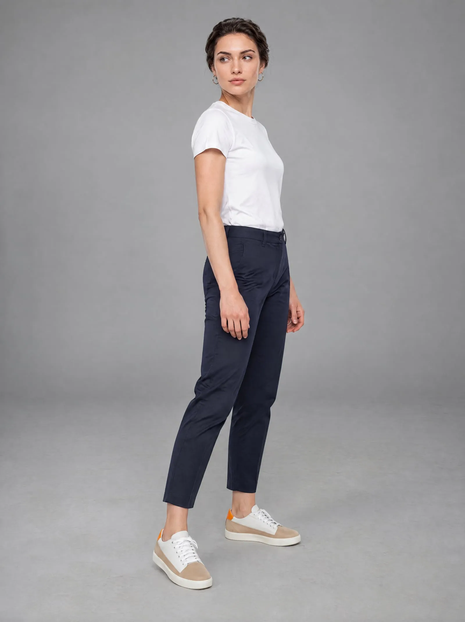 Iris wearing the sand suede court sneakers, with one foot forward, in a grey studio