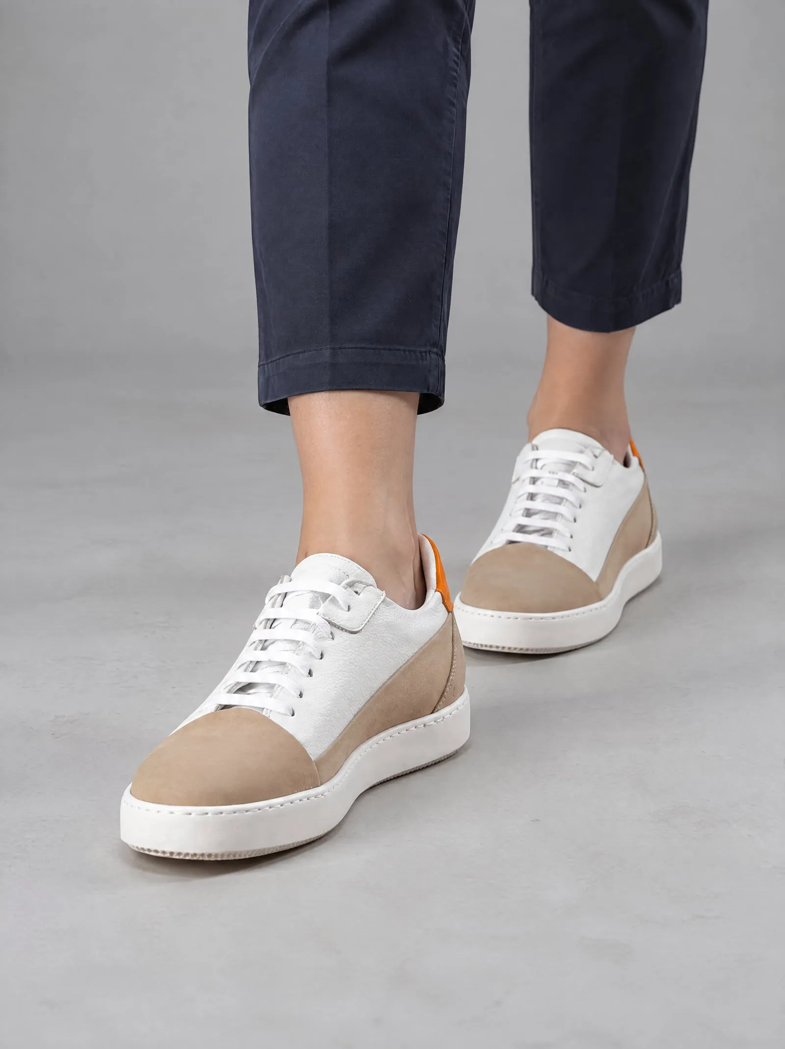 Iris wearing the sand suede court sneakers, stepping forward, in a grey studio