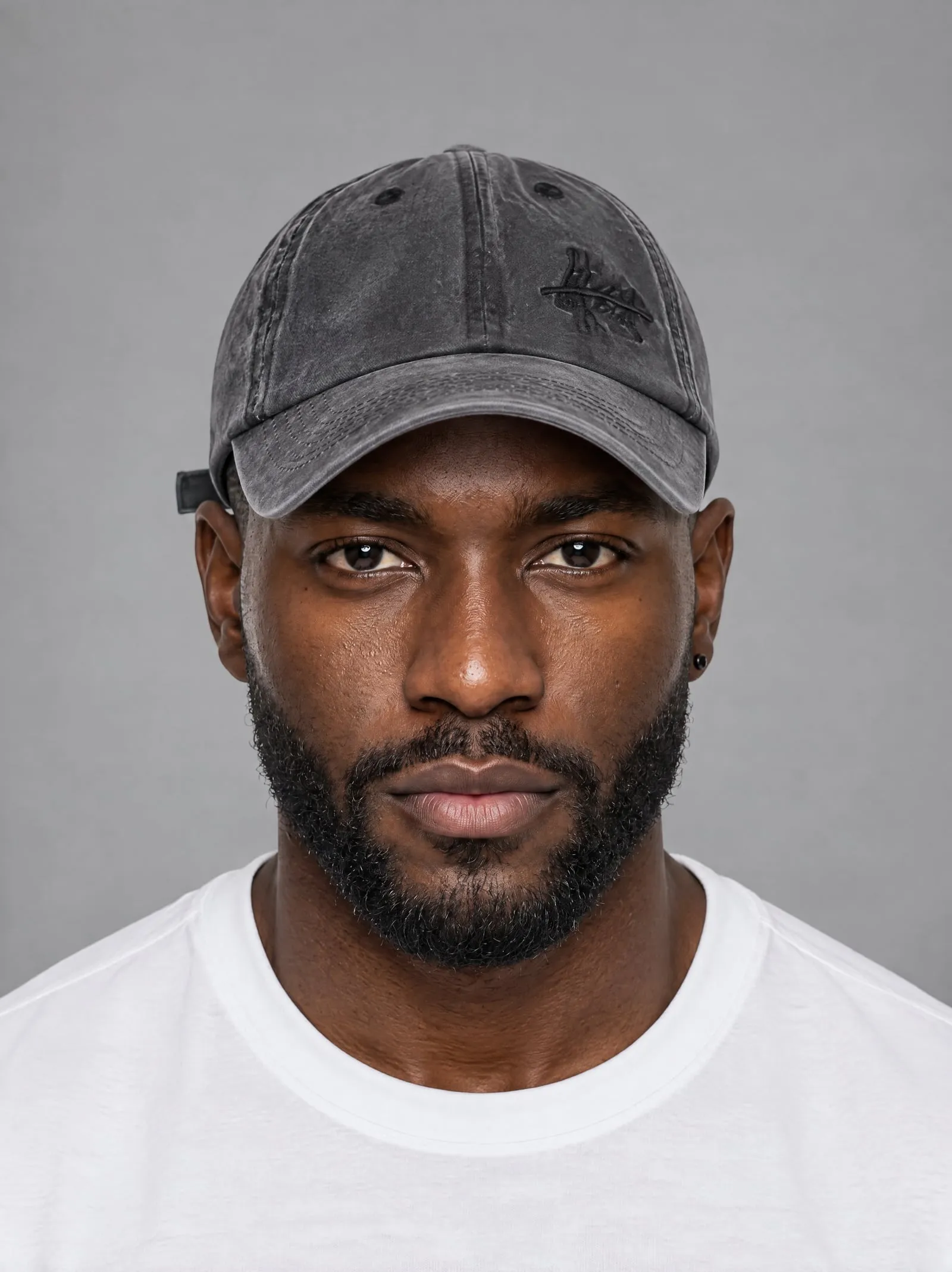 Malik wearing the washed charcoal cap, in a portrait, in a grey studio