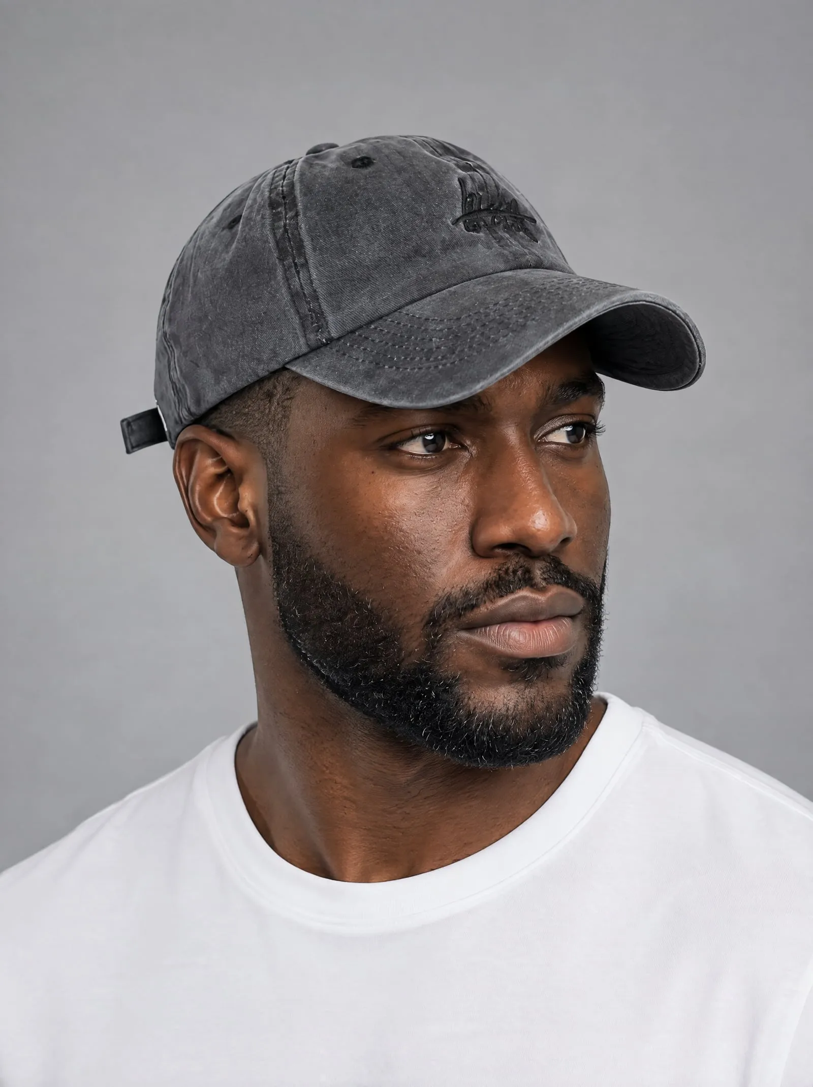Malik wearing the washed charcoal cap, at three-quarter view, in a grey studio