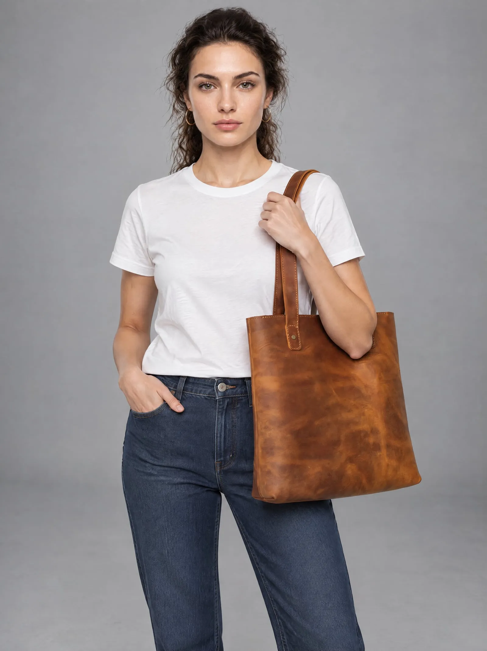Mira wearing the tan leather tote bag, carrying it on her shoulder, in a grey studio