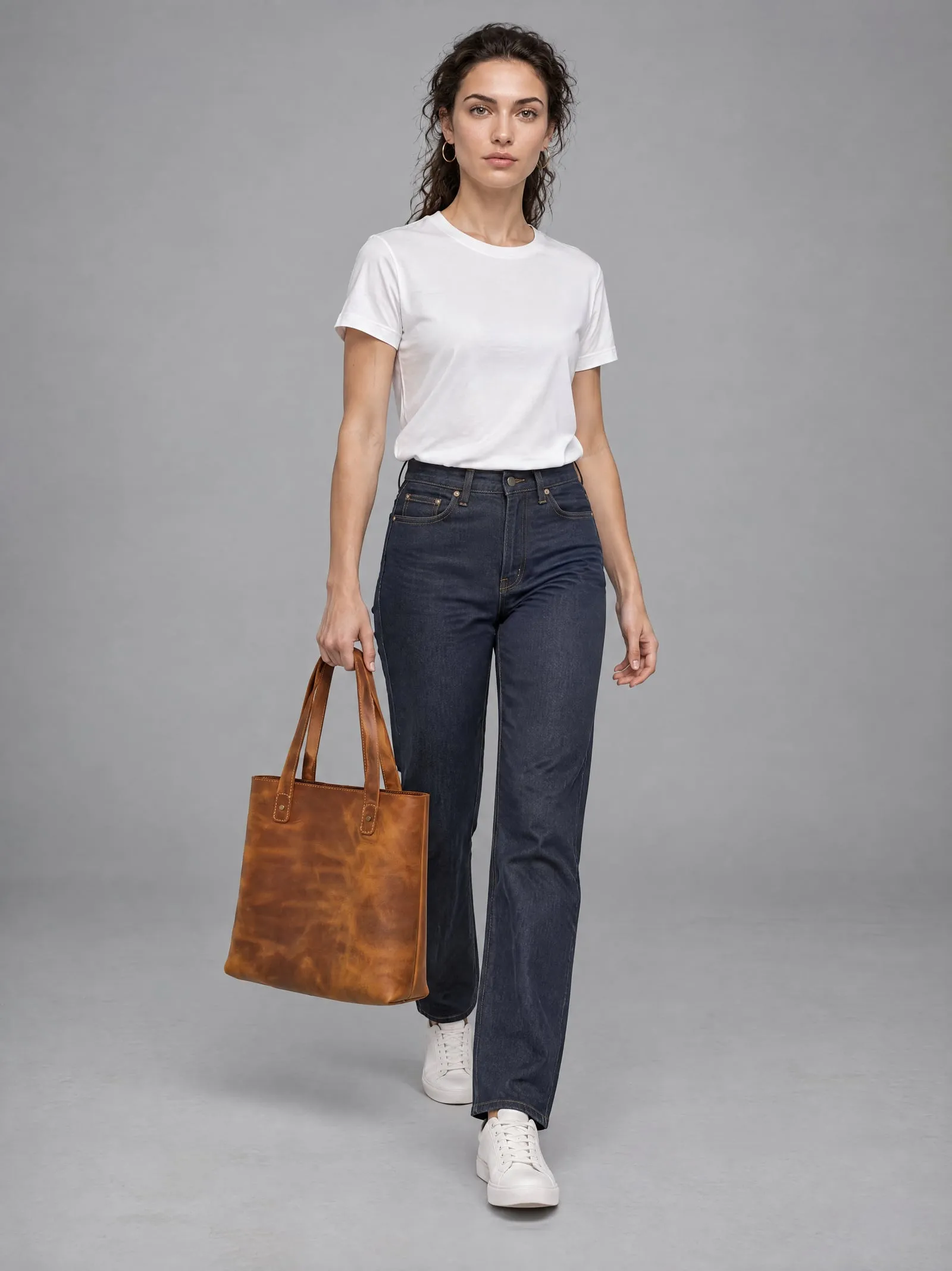 Mira wearing the tan leather tote bag, walking, in a grey studio