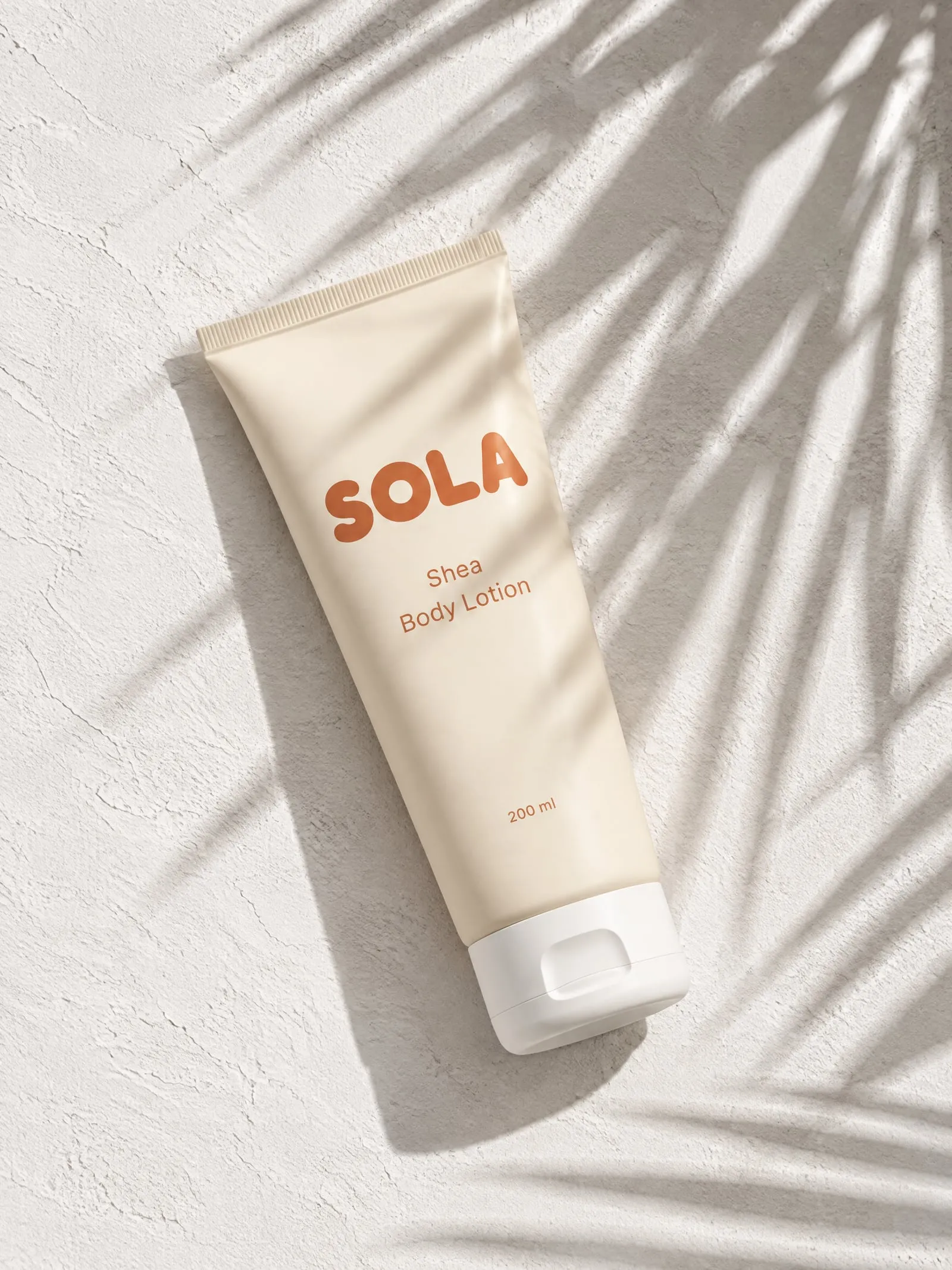 The SOLA shea body lotion, from above, in hard sun and leaf shadows