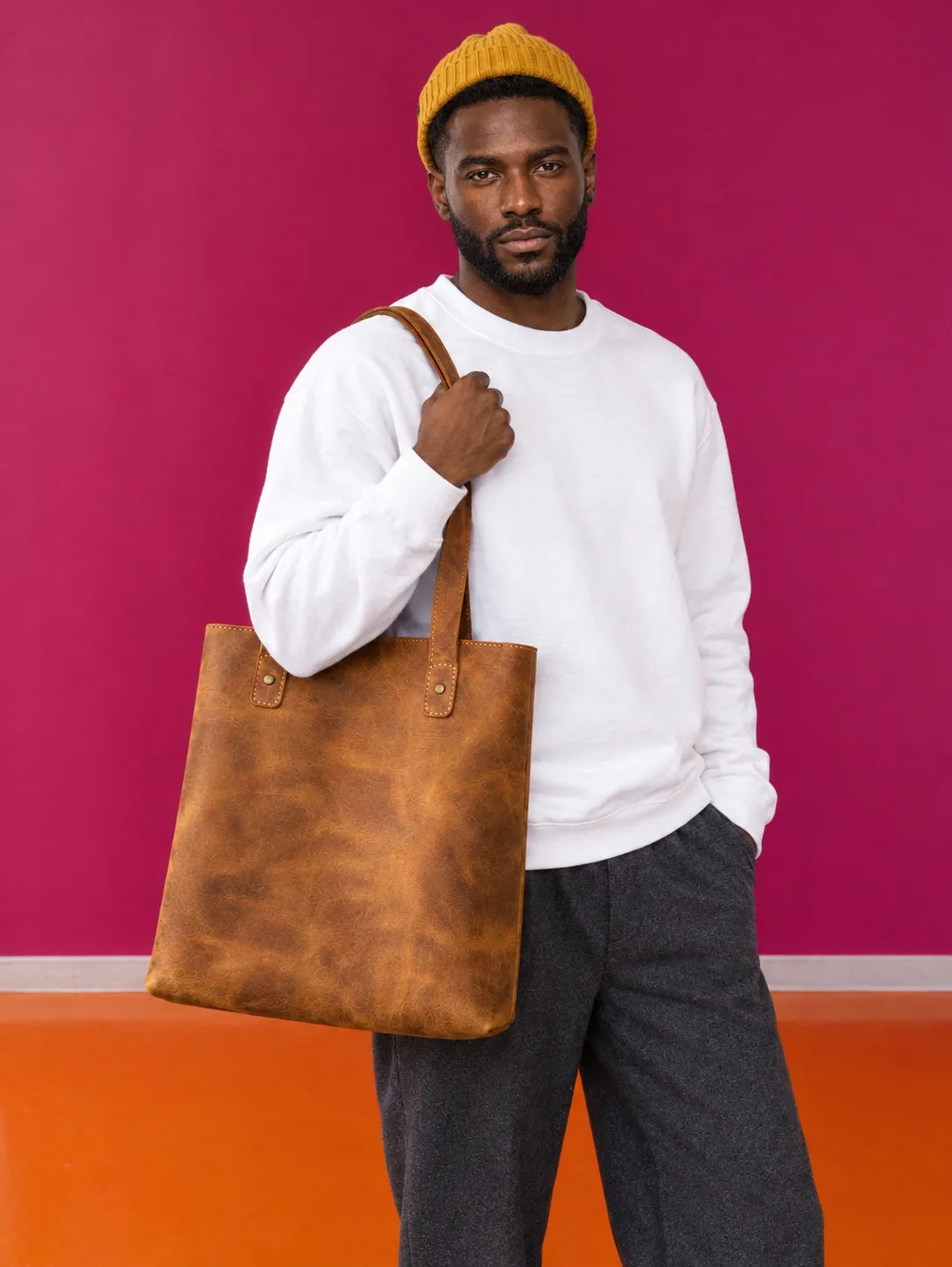 Malik wearing the white sweater and mustard beanie with the tan tote, against the magenta wall